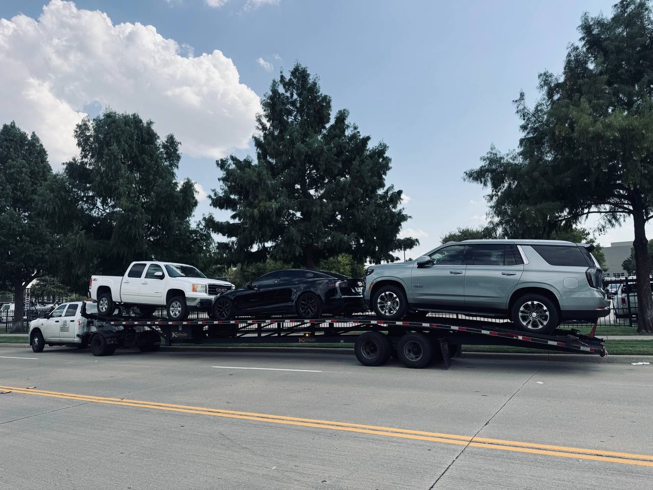 GMC truck, Tesla, and Chevy Tahoe on open car hauler